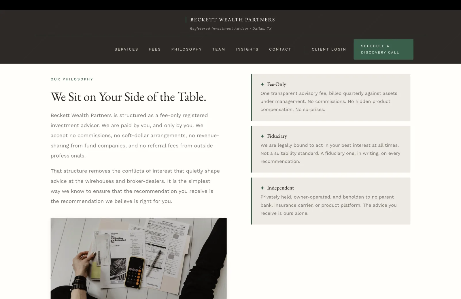 Philosophy section: a calm cream field with a split layout. Left column carries a small green caps eyebrow reading OUR PHILOSOPHY, then a tall serif headline 'We Sit on Your Side of the Table.' Two body paragraphs follow. Paragraph one: 'Beckett Wealth Partners is structured as a fee-only registered investment advisor. We are paid by you, and only by you. We accept no commissions, no soft-dollar arrangements, no revenue-sharing from fund companies, and no referral fees from outside professionals.' Paragraph two: 'That structure removes the conflicts of interest that quietly shape advice at the wirehouses and broker-dealers. It is the simplest way we know to ensure that the recommendation you receive is the recommendation we believe is right for you.' Beneath the paragraphs, a calm editorial photograph fills the lower-left quadrant: a top-down shot of an off-white wood table covered with personal-finance documents in a casual planning session, including a 1040 instruction booklet titled Tax Withholding and Estimated Tax for 2019, a few open file folders, an iPhone resting on a yellow Post-it pad, a black sleeve, and a hand at the lower edge of the frame. Right column on the same cream field carries three stacked horizontal cards each with a green left rule and a small green diamond icon. Card one Fee-Only: 'One transparent advisory fee, billed quarterly against assets under management. No commissions. No hidden product compensation. No surprises.' Card two Fiduciary: 'We are legally bound to act in your best interest at all times. Not a suitability standard. A fiduciary one, in writing, on every recommendation.' Card three Independent: 'Privately held, owner-operated, and beholden to no parent bank, insurance carrier, or product platform. The advice you receive is ours alone.'